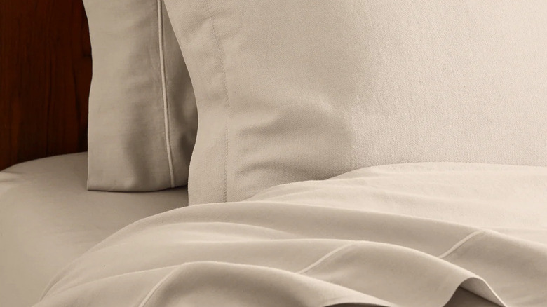 Riley cotton cashmere sheets and pillowcases on a bed with a wood headboard in the background