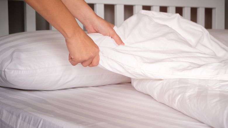 Person pulling at the corner of white sheets on a bed with a slatted headboard in the background