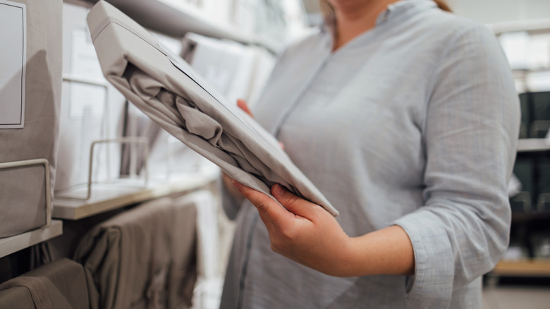 Woman looking at a set of sheets in a store with a display of sheets behind her