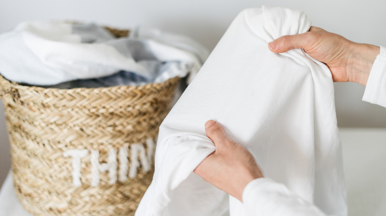 Person holding a white sheet with a laundry basket in the background