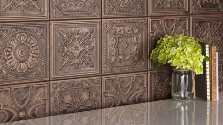 Stamped bronze tile backsplash behind a stone counter with a vase and books
