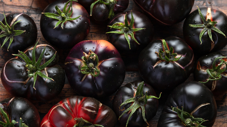 Freshly harvested and washed black beauty tomatoes sit on a wooden counter.