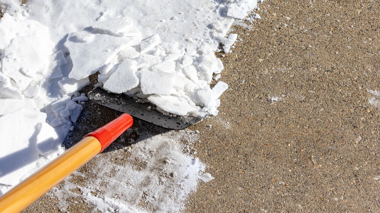 Person removing icy snow from ground with an ice scraper