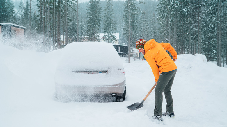 Person in a yellow jacket clearing snow with a shovel in front of a car
