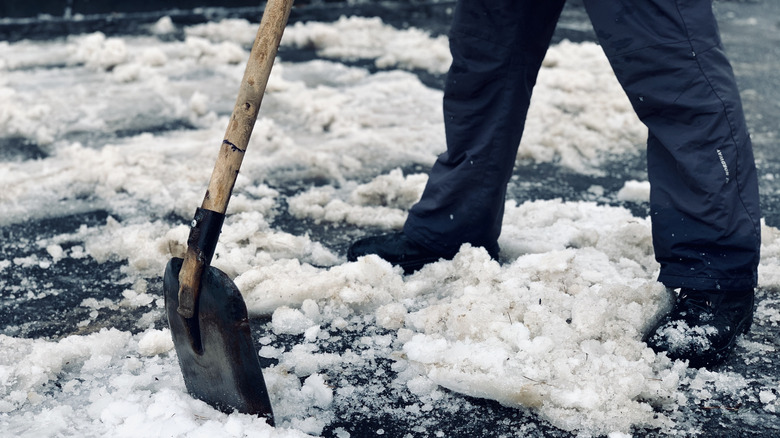 Person in dark clothing uses a metal shovel to scrape and break apart ice