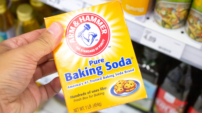 Hand holding a box of Arm & Hammer baking soda up in a store aisle