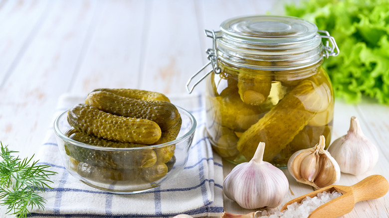 Jar of pickles in a homemade brine next to garlic cloves, and dish of pickles