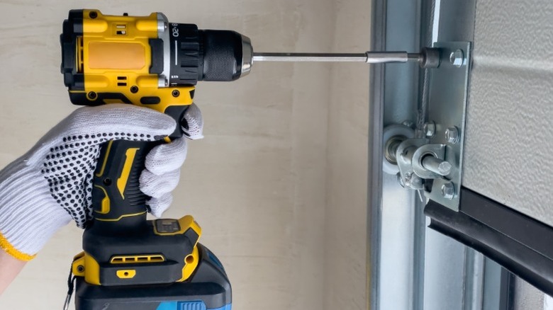 Gloved hand using power drill to tighten screws on garage door