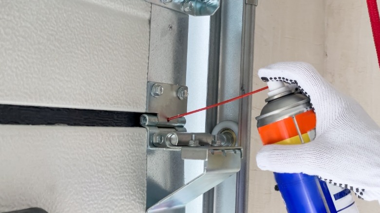 Gloved hand spraying lubricant on garage door parts