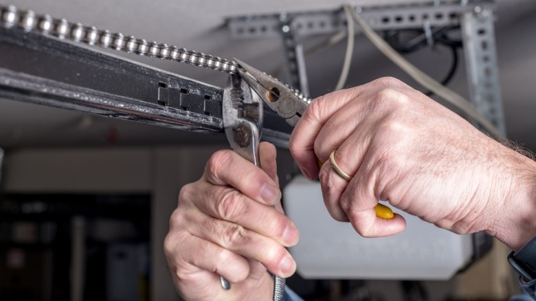 Hands repairing a garage door chain with pliers