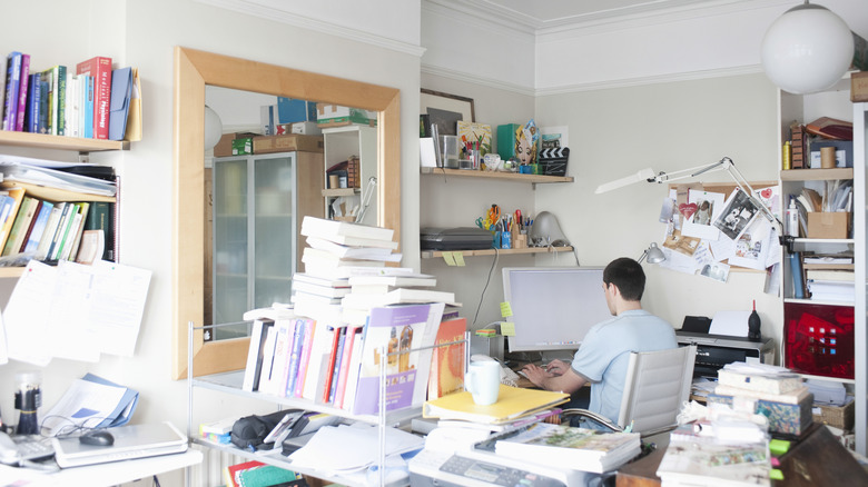 A cluttered home office space with a large mirror on the wall