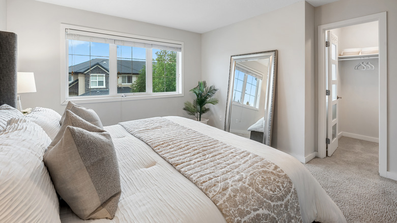 Neutral-toned bedroom with a large mirror on the floor and leaning against the wall opposite the foot of the bed