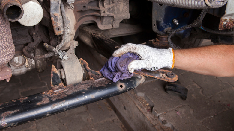 person cleaning rusted area surrounding bolts on car