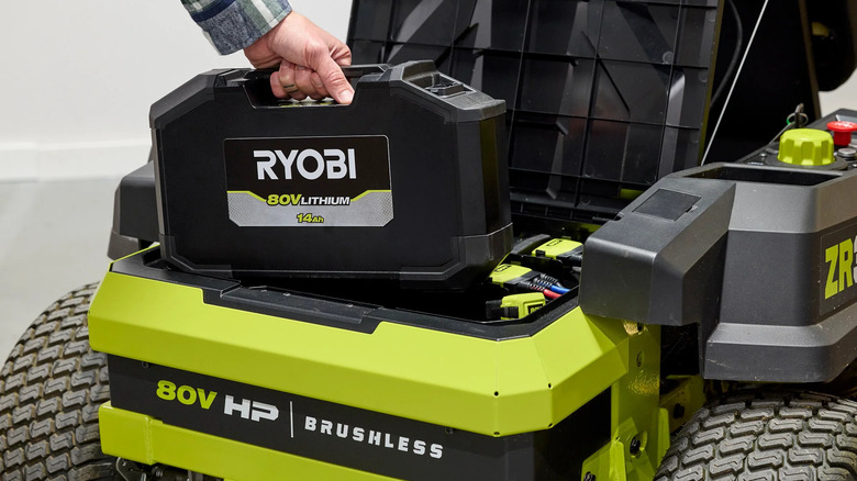 Man placing the 14Ah 80V Lithium Ryobi battery into his electric lawn mower