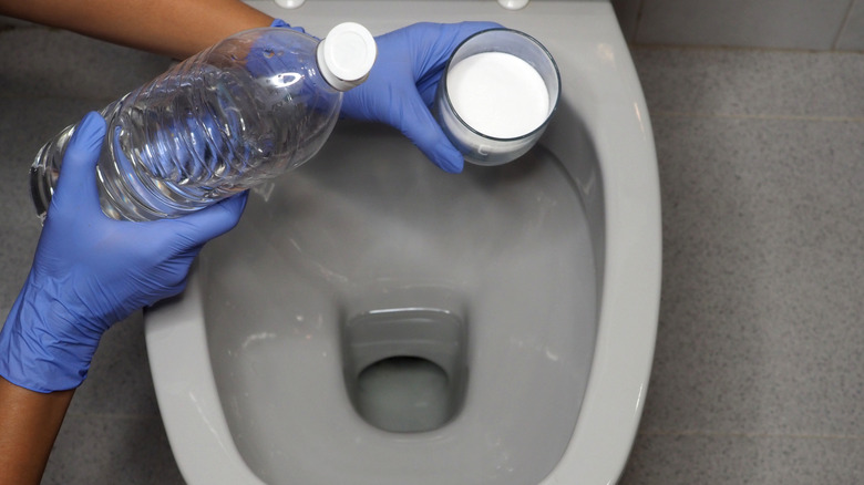 Hands preparing to pour baking soda and vinegar in a toilet.