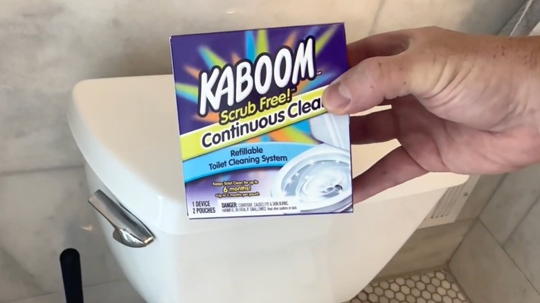Kaboom Scrub Free! Continuous Clean Toilet Cleaning System held in front of a toilet.