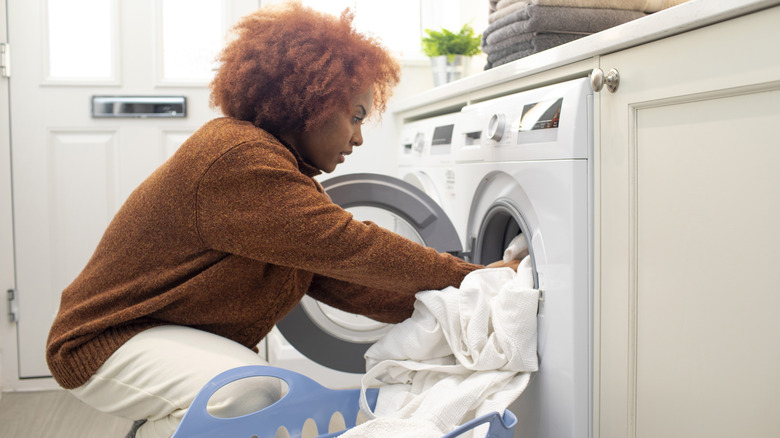 A lady putting sheets into a front loading washing machine.