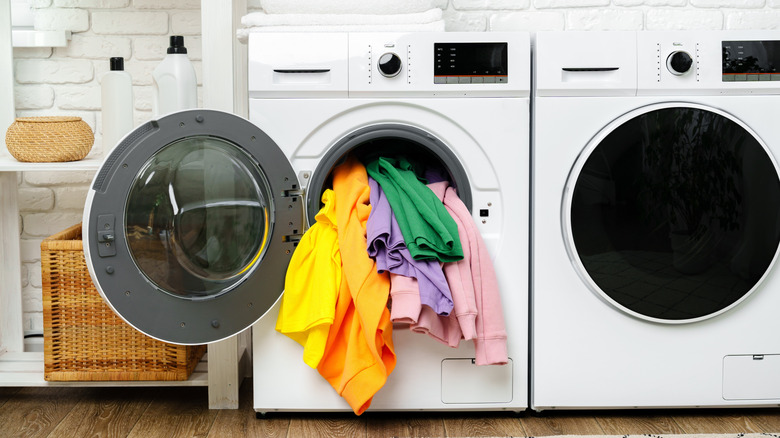 Overly full washing machine with clotes hanging out of it next to a  tumble dryer with door closed.