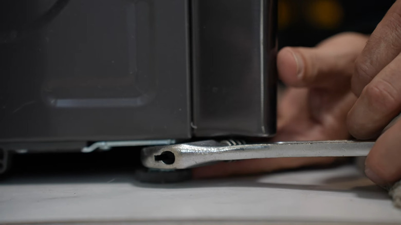 A person adjusting the feet of a vibrating washing machine