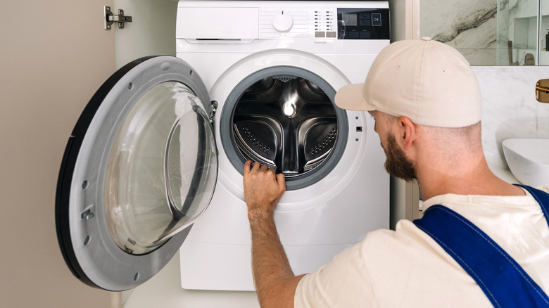 A repair man checking the drum of a washing machine in a bathroom cupboard.