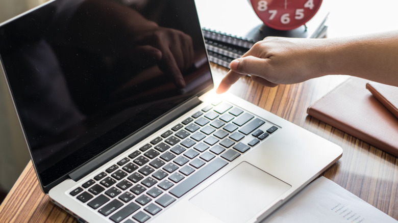 A finger lingering over the power button on a laptop keyboard.