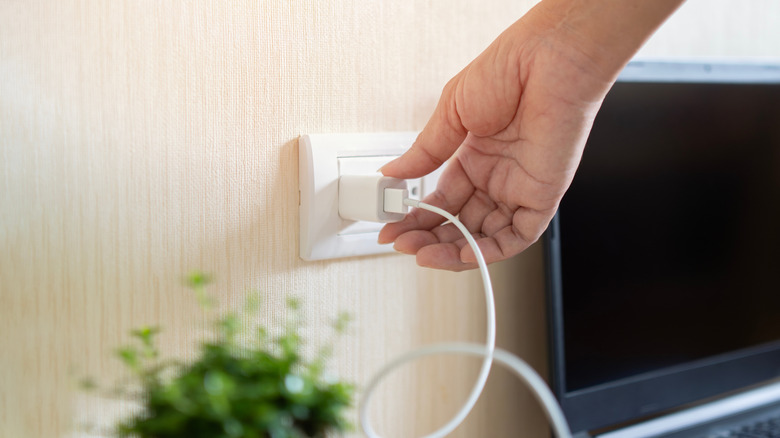 A hand unplugging a smartphone charger from a wall outlet.