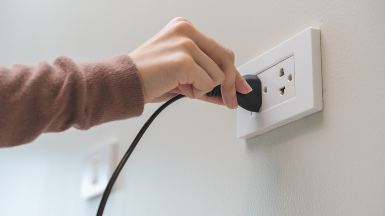 A hand unplugging cord from an electrical outlet.
