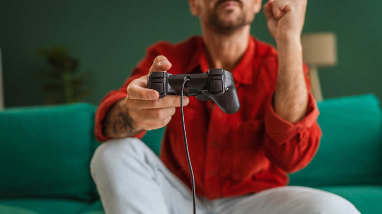 A man sits on green sofa while holding video game controller.