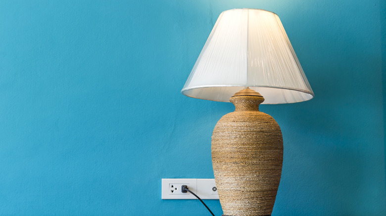 A plugged-in table lamp against a turquoise wall.