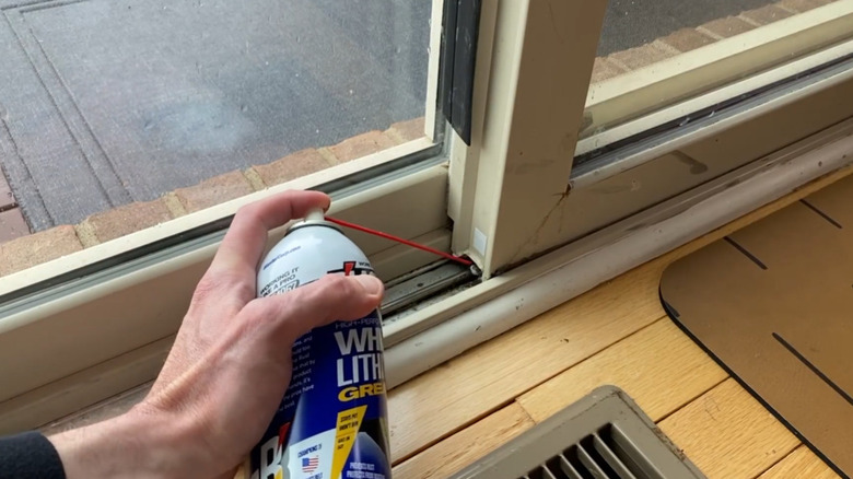 A hand using a can of WD40 to lubricate the tracks of a sliding glass door.