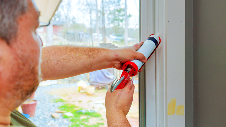 A man using a caulking gun to reseal the door frame.