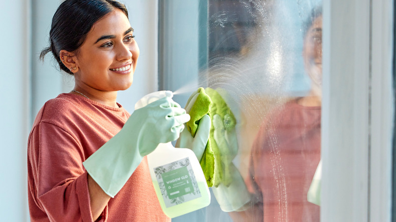 A smiling woman wiping down the glass of sliding glass doors.