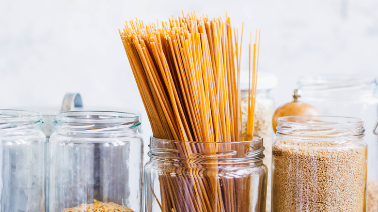 Spaghetti sticking out of a glass jar next to dry goods in other jars
