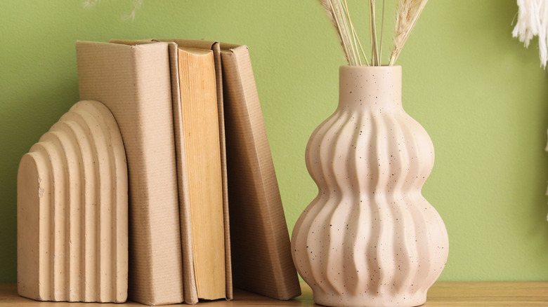 Avant garde ceramic vase filled with grasses next to stack of books on shelf with earthy decor