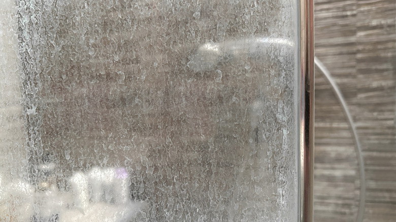 Closeup of a shower door covered in stains and hard water buildup