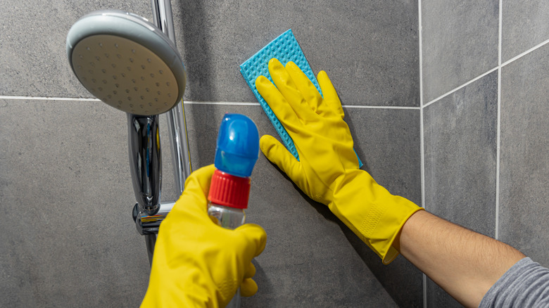 Closeup of person cleaning shower walls with sponge