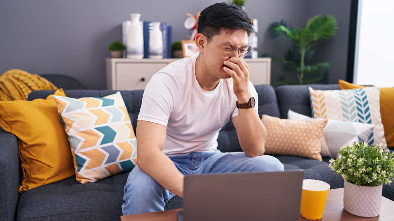 Asian man holds nose while sitting on a couch