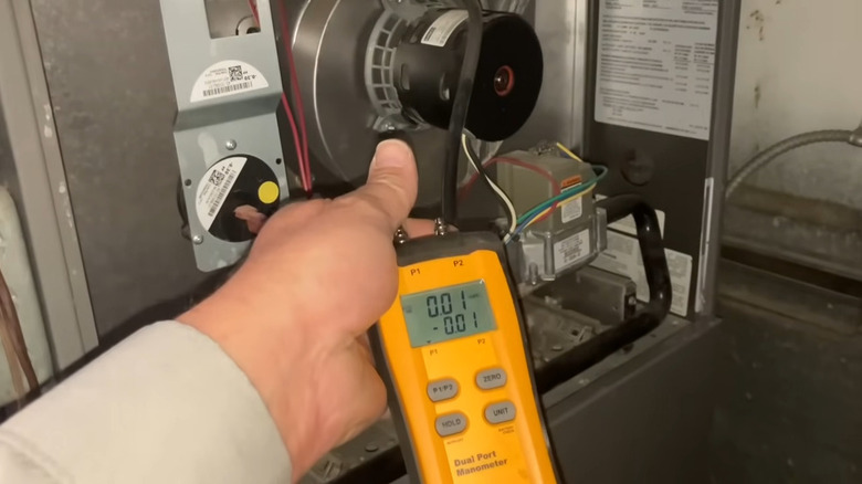 HVAC tech holding a digital manometer to detect a cracked heat exchanger in a furnace
