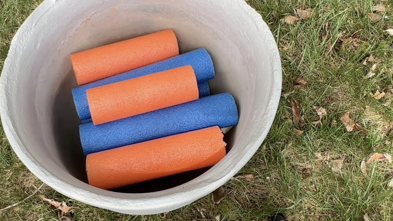 A large plastic planter on a lawn filled with cut up orange and blue pool noodles.