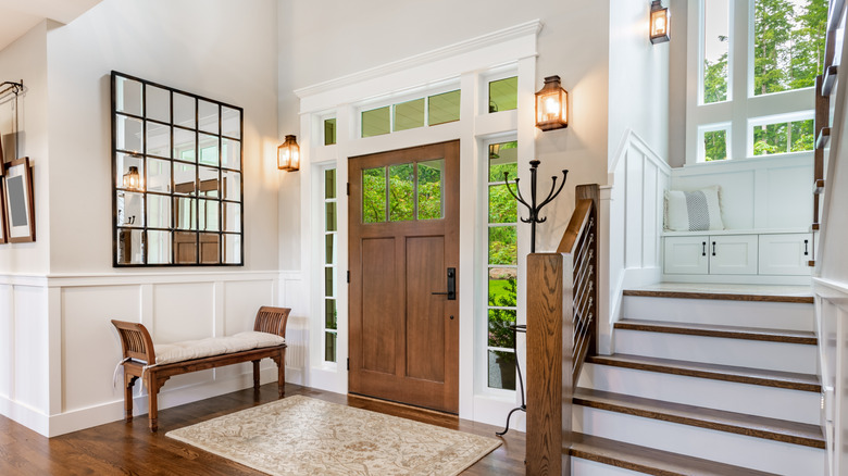 Front entry foyer of a luxurious home rich wood tones staircase bench with a welcoming feel