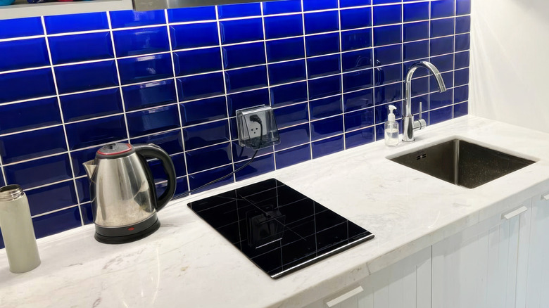 Blue kitchen backsplash surrounded by a white countertop sink and cabinetry