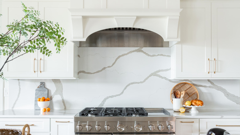 A panel of stone covering the backsplash of an all white kitchen