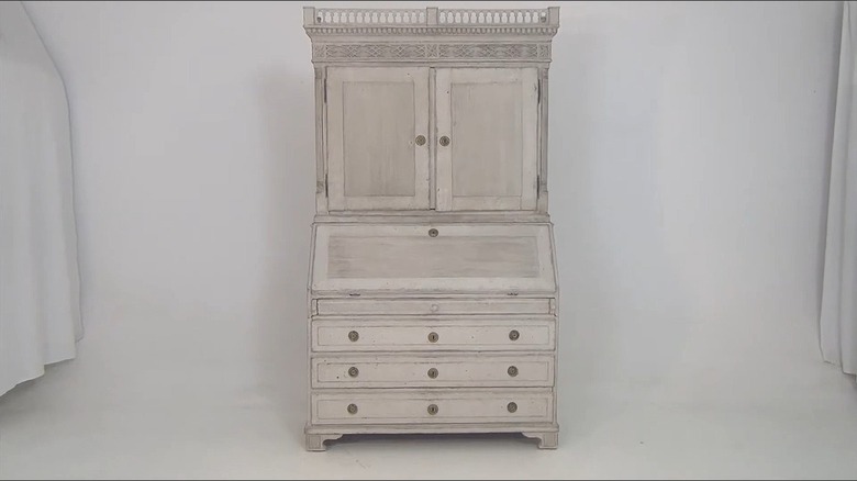 Armoire in the Gustavian style with light finish and simple, symmetrical design along the top edge