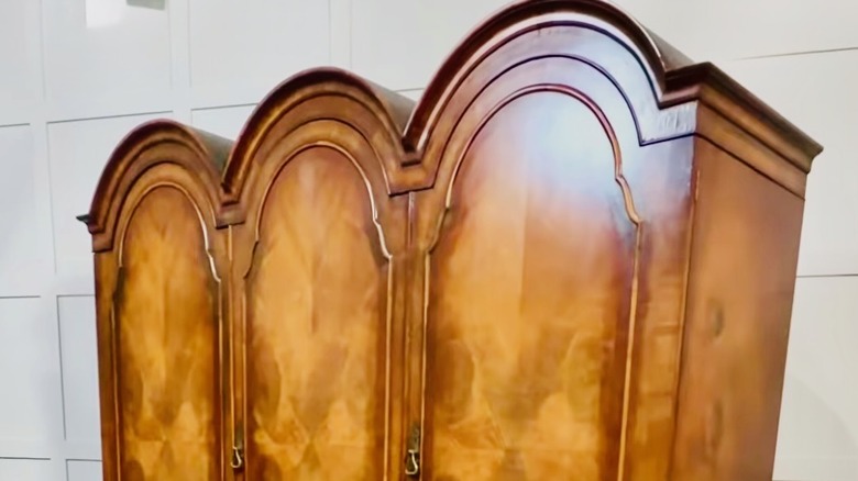 A three-section armoire in the Queen Anne style with curves along the top and lighter wood on the doors