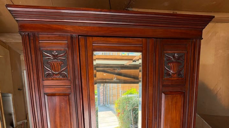 Mirrored Victorian armoire with two carved designs and a rich wood finish
