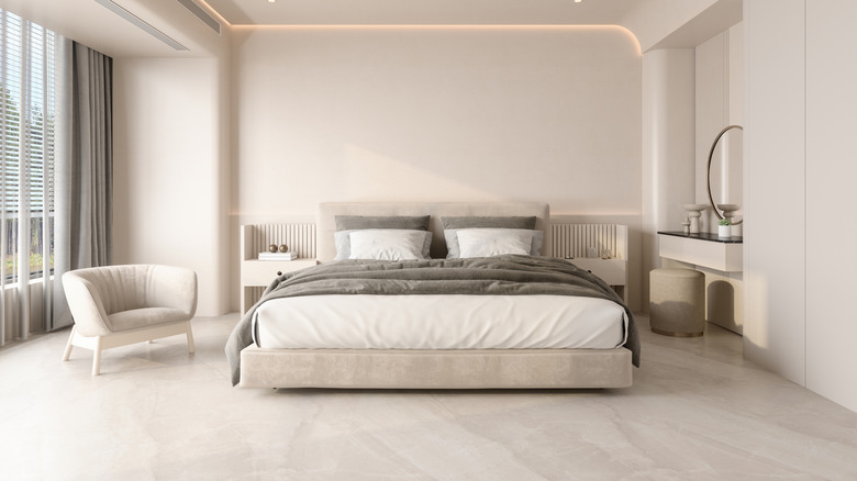 A cream painted bedroom with cream bed, a grey blanket and cream armchair.