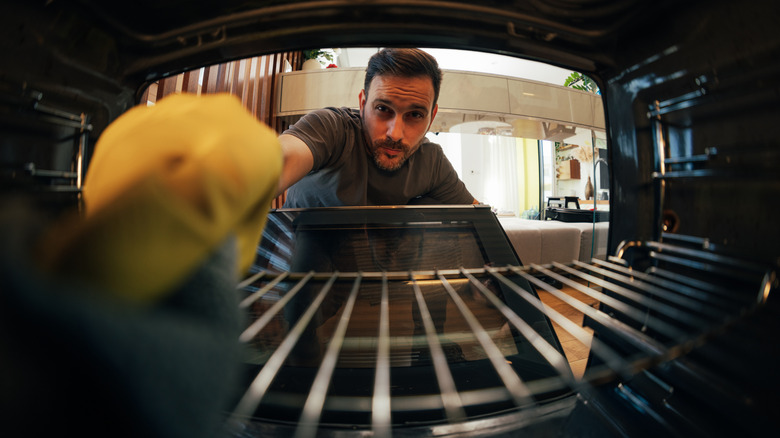 man carefully cleans oven interior