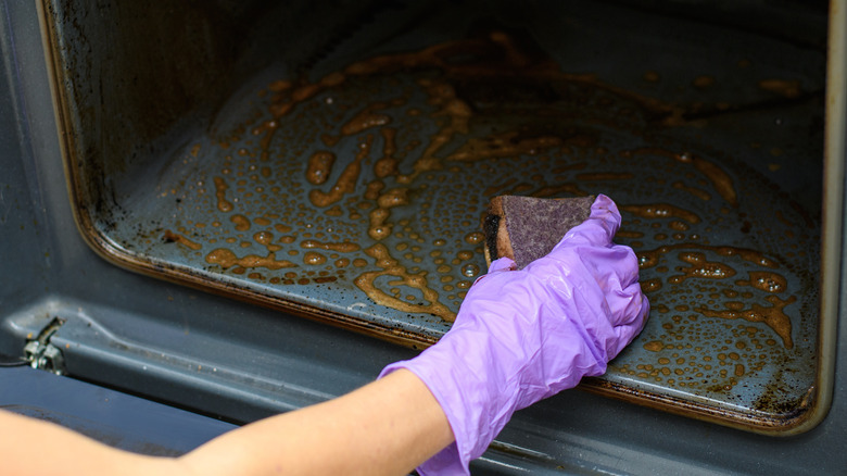 Someone scrubbing a dirty oven with a sponge and cleaner