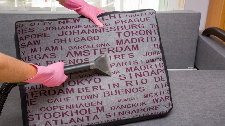 Pink gloved hands vacuuming decorative pillow on couch