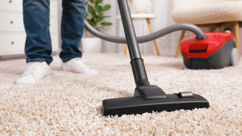 Person vacuuming light colored carpet in bedroom